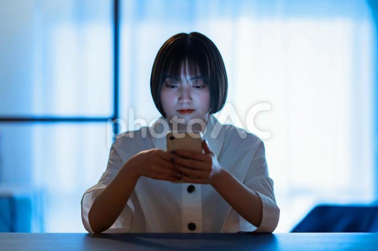 厳しい表情でスマートフォンを見つめる女性  スマホ,スマートフォン,snsの写真素材