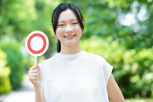 白いノースリーブの女性がマルカードをもって見せるの写真