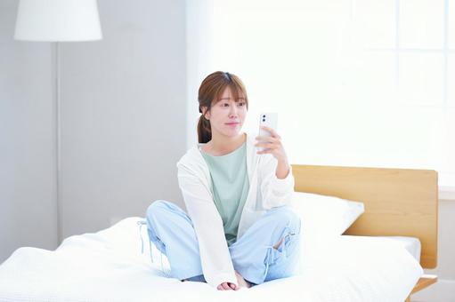 ベッドに座り片手でスマホを持ち見る女性 女性,スマートフォン,持つの写真素材
