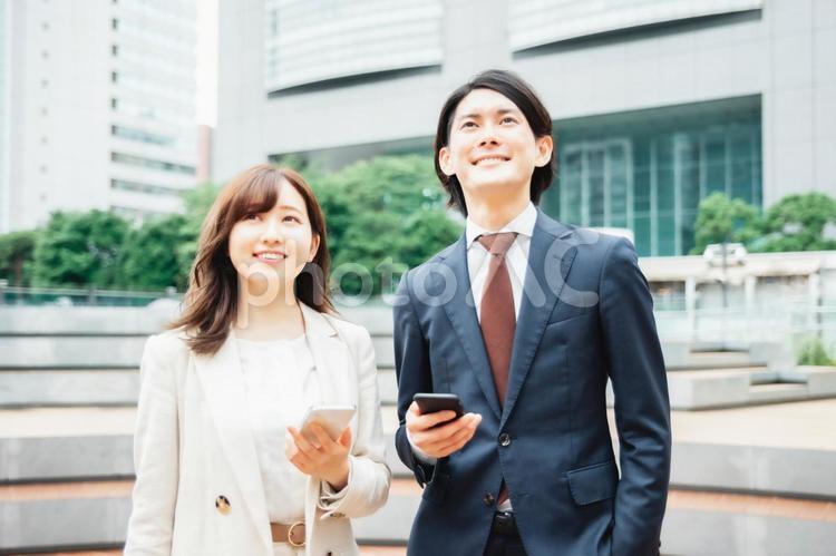スマホを持って話をするスーツ姿の男女 スマートフォン,ビジネス,アプリの写真素材