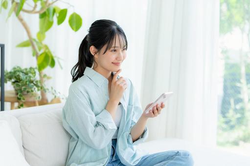 部屋でスマホを操作する若い女性 スマホ,笑顔,女性の写真素材