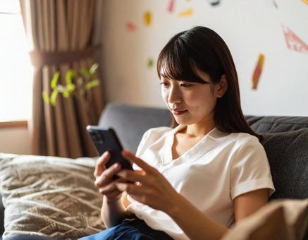 自宅のリビングでスマホを操作する女性 自宅のリビングでスマホを操作する女性の写真
