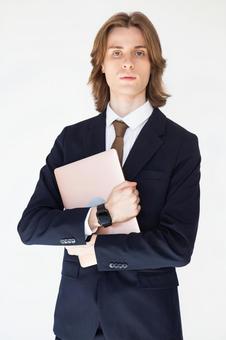 ノートパソコンを両手で抱えるカメラ目線のスーツの男性 男性,外国人,欧米人の写真素材