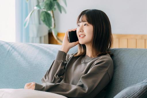 ソファに座ってスマホで話す笑顔の女性 女性,スマホ,スマートフォンの写真素材