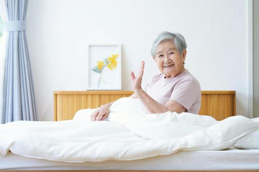 ベッドで手をあげる笑顔の高齢女性 女性,手を振る,手をあげるの写真素材