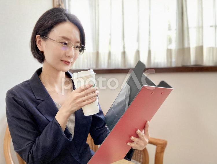 バインダーを持ちながらコーヒーを飲む女性 女性,スーツ,笑顔の写真素材