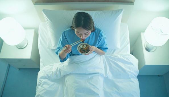 入院ベッドでご飯を食べる女性患者の写真
