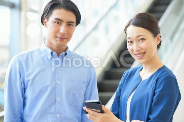 スマホを見ながら話をする2人のオフィスワーカー ビジネスマン,ビジネスウーマン,会社員の写真素材