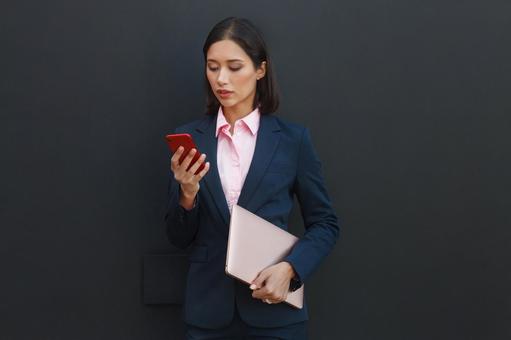 オフィスビルの外でタブレットを持ちスマートフォンを使っているビジネスウーマン ビジネスウーマン,ビジネス,女性の写真素材