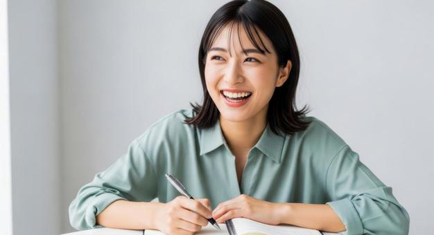 ノートを書きながら笑顔を見せる女性 ノートを書きながら笑顔を見せる女性の写真