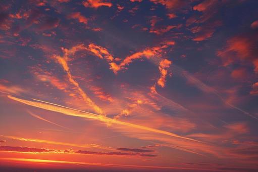 夕焼けの空に浮かぶハートの飛行機雲の写真