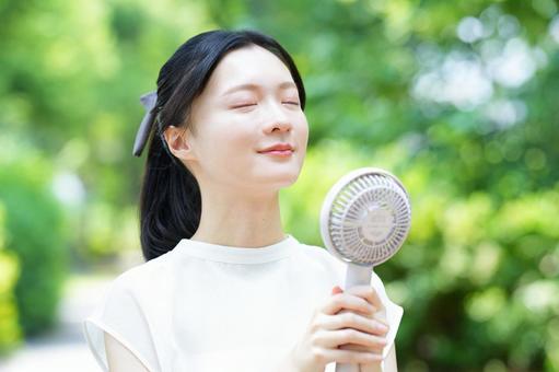 白いノースリーブの女性が公園でハンディファンを持つの写真