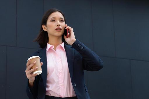 オフィスビルの外でコーヒー片手に電話している外国人ビジネスウーマン ビジネスウーマン,ビジネス,女性の写真素材