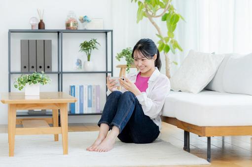 部屋でスマホを操作する若い女性 スマホ,笑顔,若い女性の写真素材