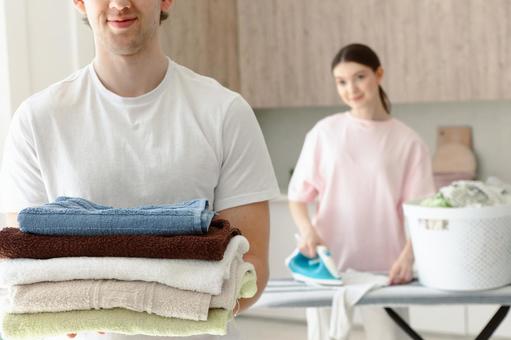 タオルを畳んで運ぶ男性とアイロンする女性 タオルを畳んで運ぶ男性とアイロンする女性 夫婦,女性,人物の写真素材