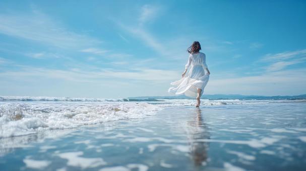 波打ち際を歩く白ワンピースの日本人女性 波打ち際を歩く白ワンピースの日本人女性の写真