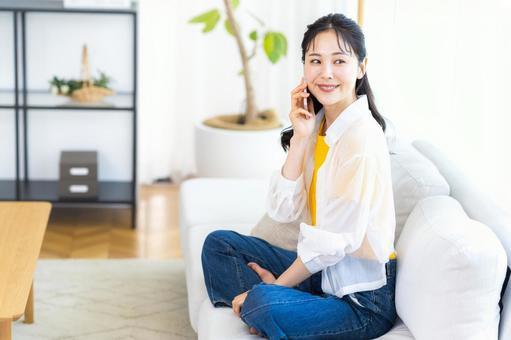 リビングでスマホで話す若い女性 スマホ,笑顔,電話の写真素材