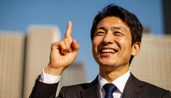 都市背景で人差し指を立てるビジネスマンの写真