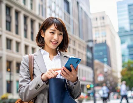 オフィス街でスマホを操作する女性社員 オフィス街でスマホを操作する女性社員の写真