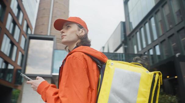 街なかでスマートフォンを手に周りを見ているフードデリバリーの男性の写真