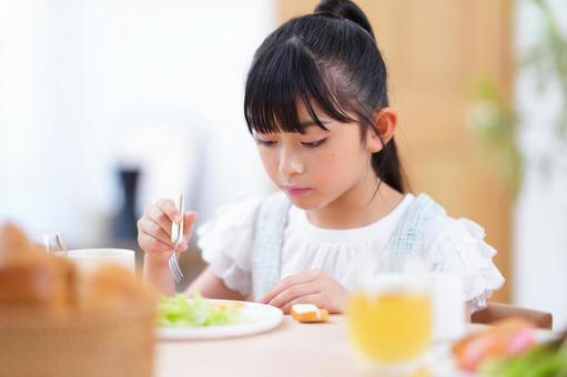 ジュースとパンが並ぶ食卓で食事を楽しむ子どもの写真