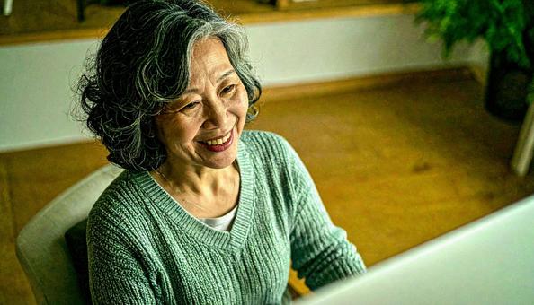 パソコンに向かって笑顔の50代の女性 パソコンに向かって笑顔の50代の女性の写真