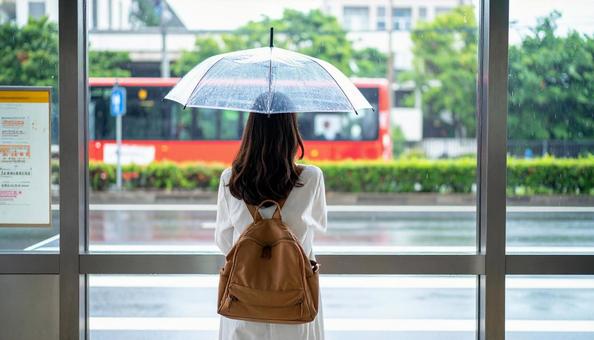 雨の中バス停でバスを待つ日本人女性の写真