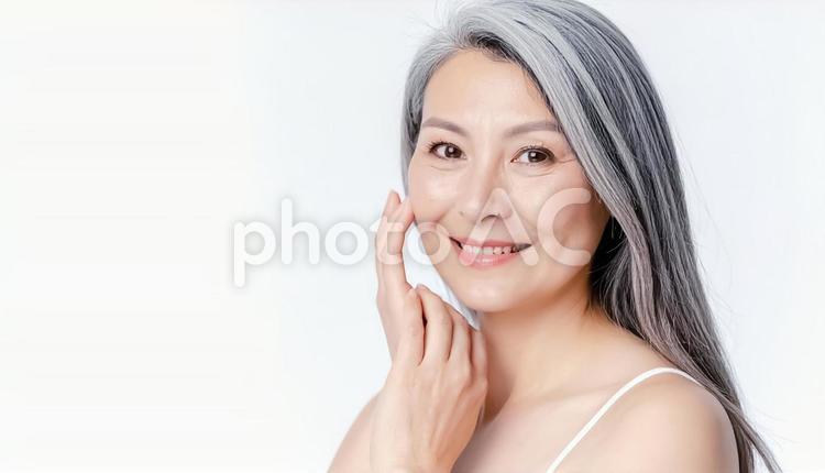 カメラ目線で頬を撫でるシニアの女性 女性,笑顔,微笑みの写真素材