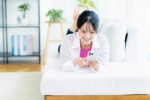 部屋でスマホを操作する若い女性 部屋でスマホを操作する若い女性 スマホ,若い女性,笑顔の写真素材