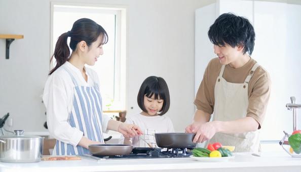 キッチンで料理を楽しむ母娘と見守る父親 キッチンで料理を楽しむ母娘と見守る父親の写真