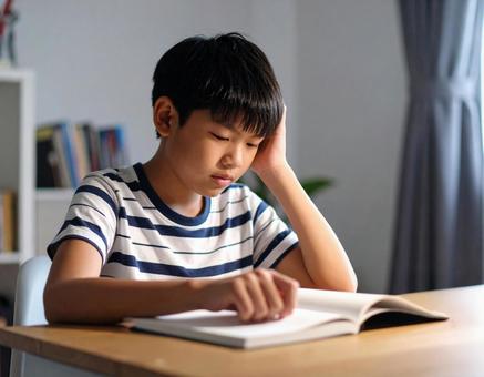 つまらなそうに本を読む子供 つまらなそうに本を読む子供の写真