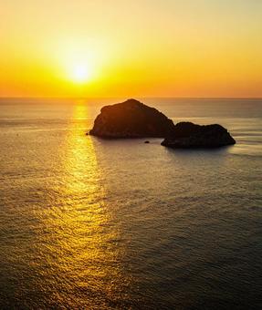 島のシルエットと朝日と海の写真