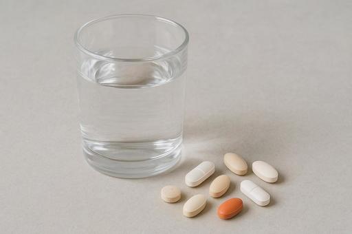 複数の錠剤と水の入ったコップの写真
