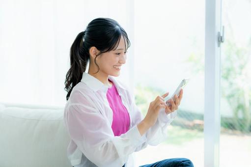 部屋でスマホを操作する若い女性 スマホ,若い女性,笑顔の写真素材