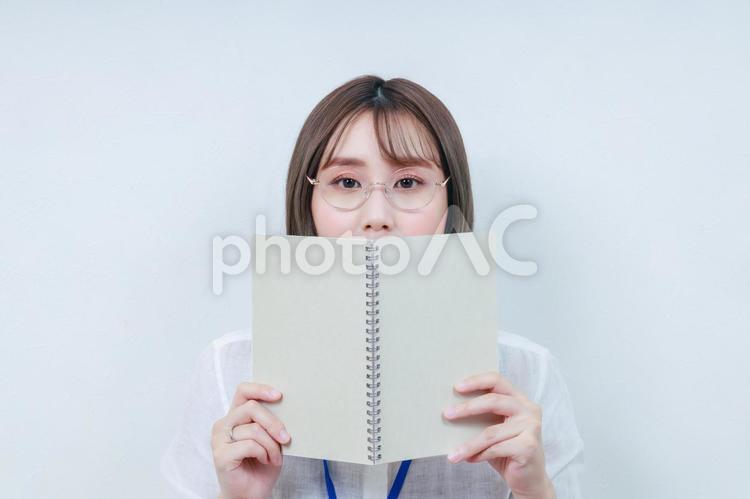 ノートで顔を隠す眼鏡をかけた若い女性 女性,女の子,若いの写真素材