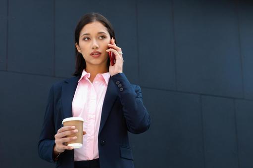 オフィスビルの外でコーヒー片手に電話している外国人女性 ビジネスウーマン,ビジネス,女性の写真素材