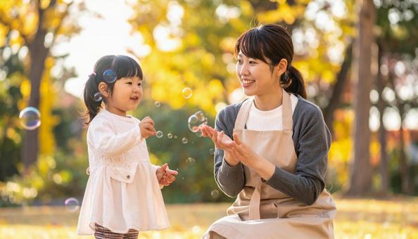 幼児教育　公園でシャボン玉で遊ぶ子と女性の写真