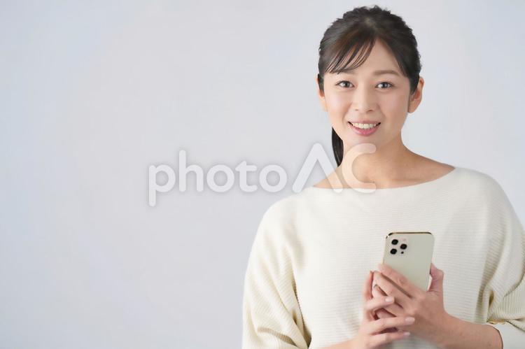 スマートフォンを持ってカメラ目線の女性（余白あり） 女性,主婦,スマートフォンの写真素材