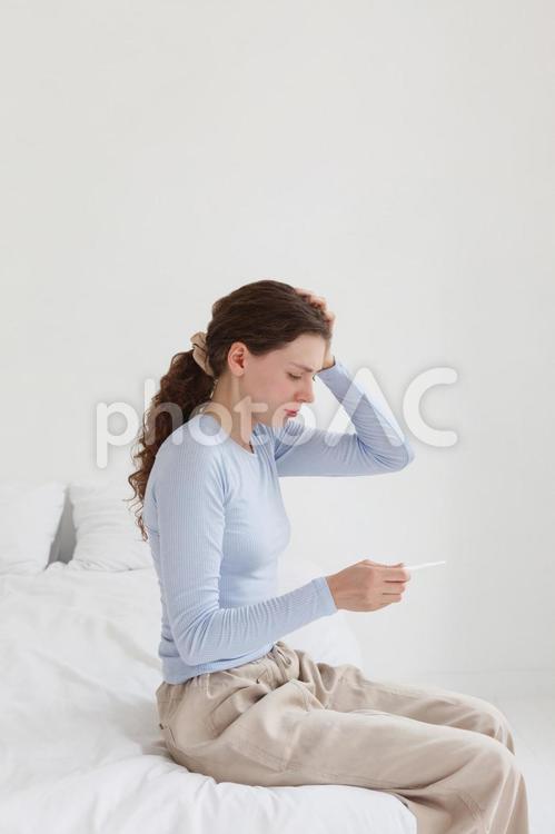 ベッドを座って体温計を見ている女性 女性,人物,座るの写真素材
