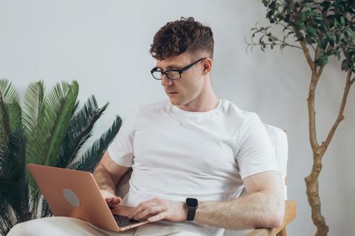 椅子に座って膝の上でノートパソコンを使うTシャツを着た男性 男性,外国人,欧米人の写真素材