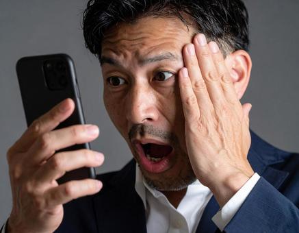 スマートフォンを見て驚く男性 スマートフォンを見て驚く男性の写真