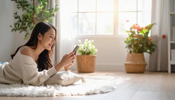 リビングで横になりスマホを操作する女性の写真