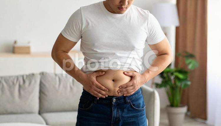 室内で自分のお腹の脂肪を気にする若い男性 人物,男性,ダイエットの写真素材