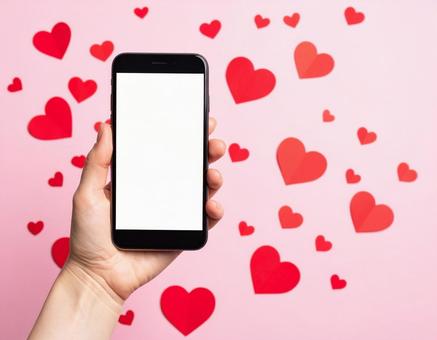 スマートフォンを持つ手とハートの背景 スマートフォンを持つ手とハートの背景の写真