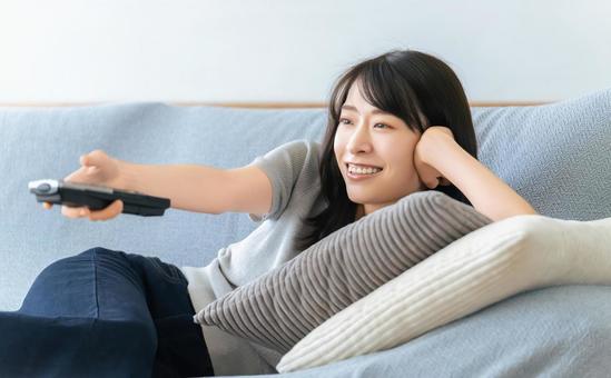 ソファに寝転んでテレビを見る女性 女性,テレビ,ソファの写真素材