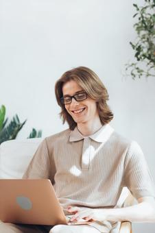 椅子に座って膝の上でノートパソコンを使う笑っている若い男性 男性,外国人,欧米人の写真素材