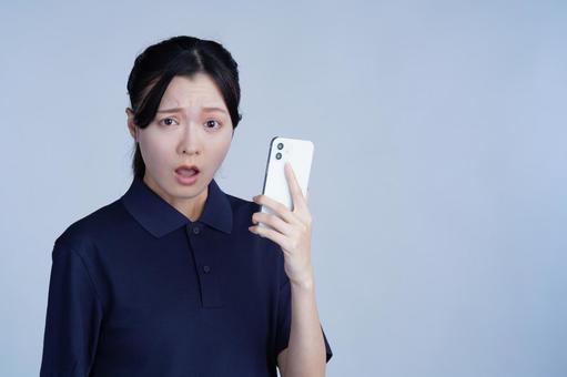 紺色の服の女性がスマホを見て驚くの写真