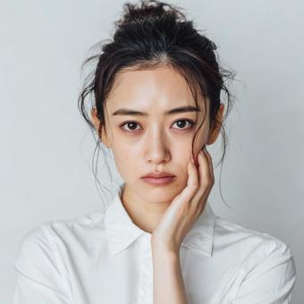 頬に手を当てて悩む若い日本人女性 頬に手を当てて悩む若い日本人女性の写真