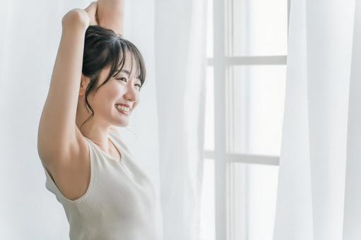 寝起きにカーテンの前で朝日を浴びる女性 寝起きにカーテンの前で朝日を浴びる女性 脇脱毛,脱毛,女性の写真素材