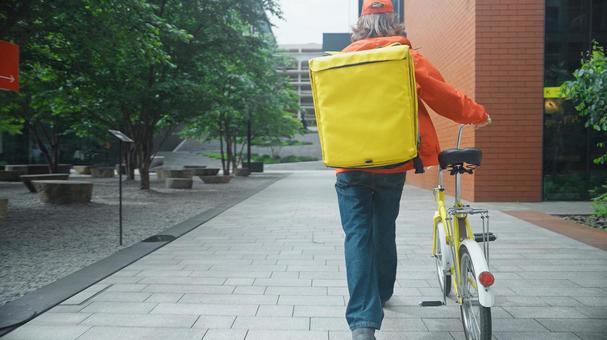 自転車を押して歩くフードデリバリーの男性の後ろ姿 配達,フードデリバリー,デリバリーの写真素材